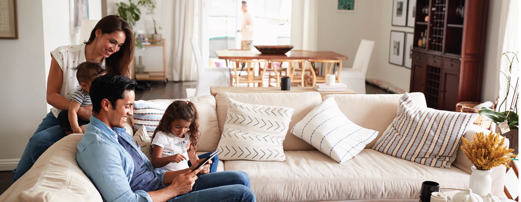 young children sit on a couch with and look at an ipad with their parents