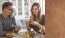 woman looks at her phone at the dining table while her husband holds a fork full of veggies 